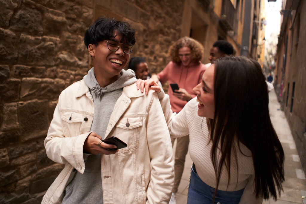 Group of happy friends using phone outdoors while walking and laughing. 