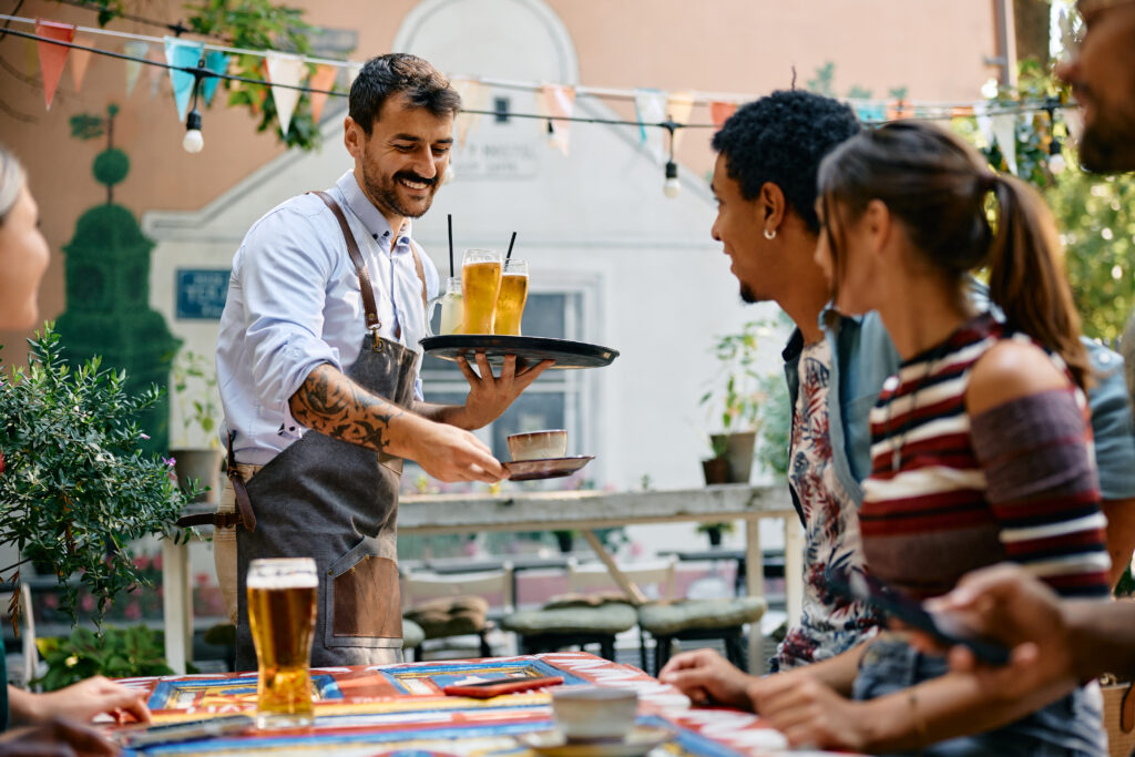 Happy waiter serving drinks to his guests while working in a cafe.