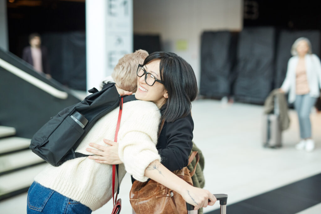 Photo of young woman greeting her friend with hug in airport.