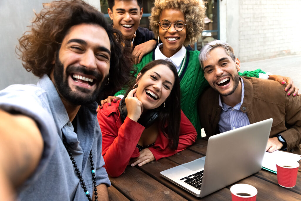 Selfie of multiracial friends looking at camera in a casual business meeting at restaurant terrace outdoors. Technology, business and friendship concept.
