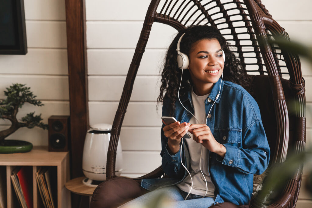 Young woman listening to the music in the rocking chair in cosy flat.
