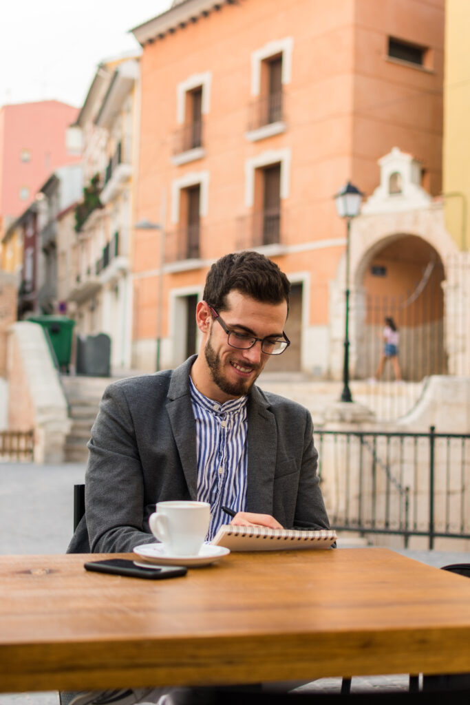 Photo of young businessman is writing in his notebook in a bar terrace.