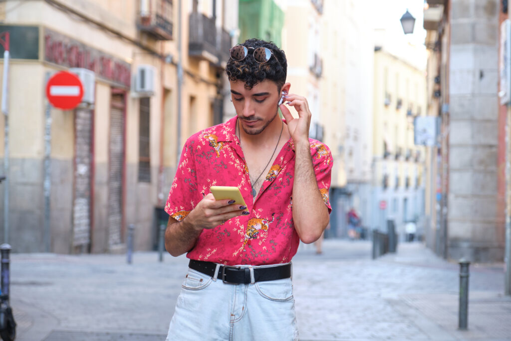 Young caucasian man with long false nails choosing a song with his smartphone at street.